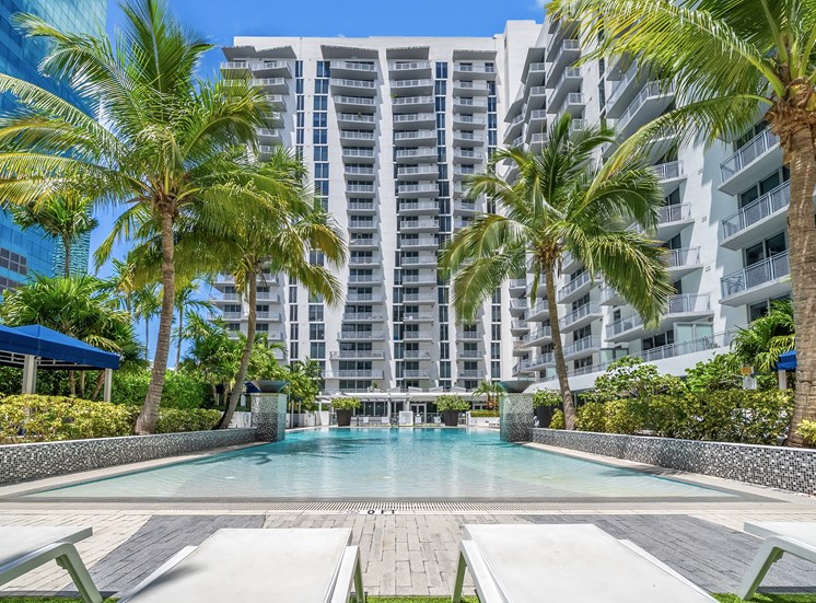 A pool surrounded by palm trees and a building in the background.